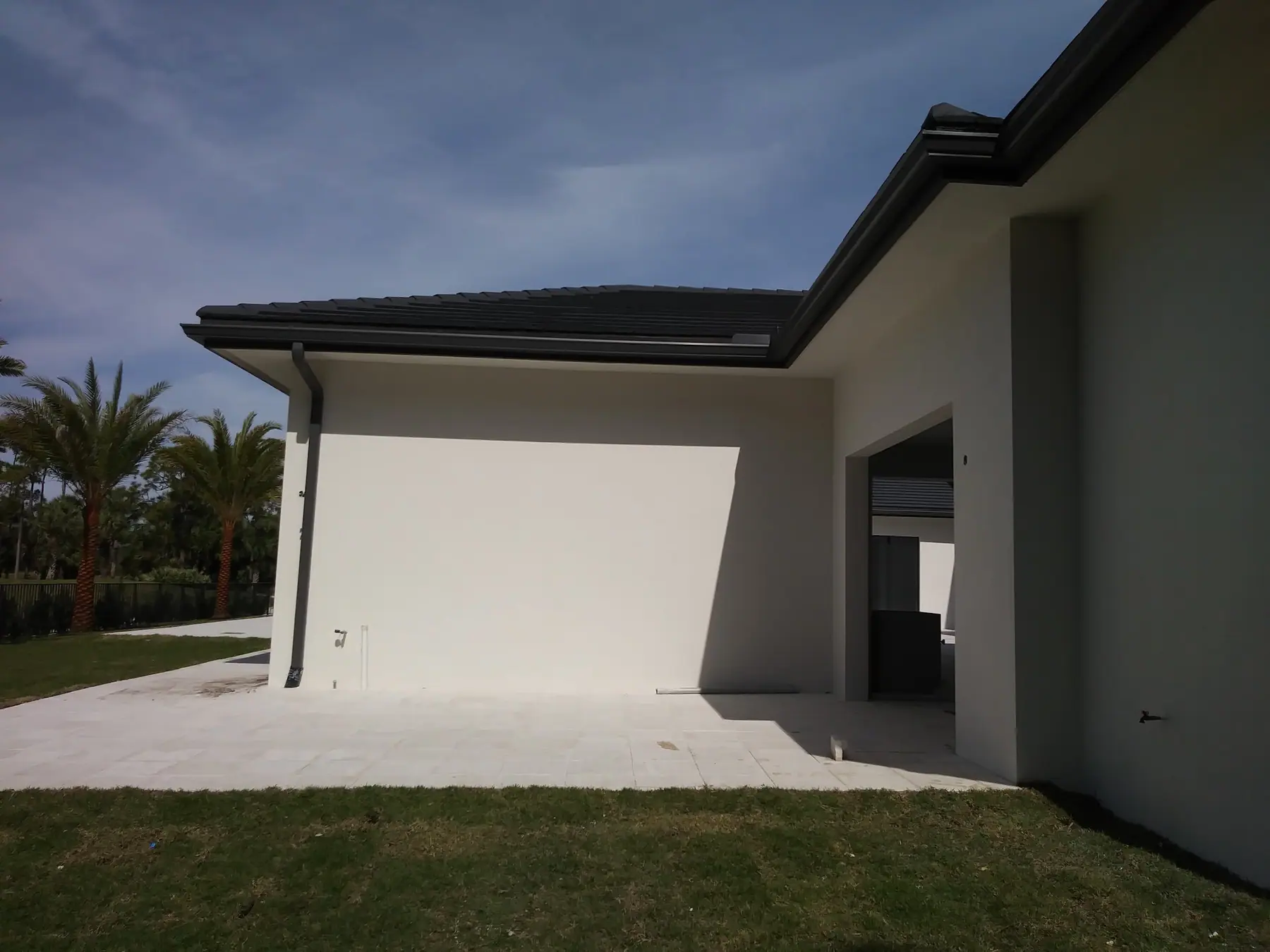 Dark bronze seamless gutters and downspout on a modern white stucco home with palms