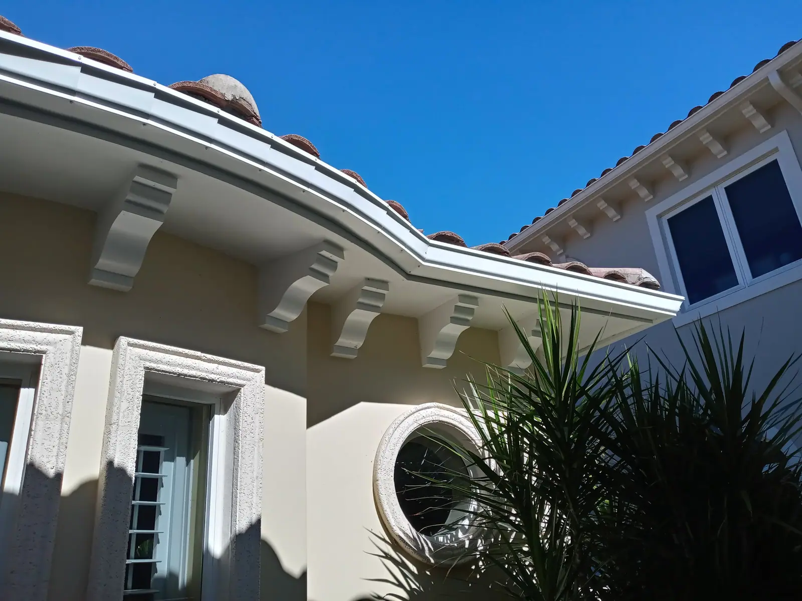 White seamless gutter following a curved tile roofline above decorative corbels