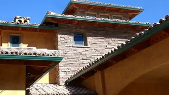Green gutters under a tile roof on a stone and stucco home