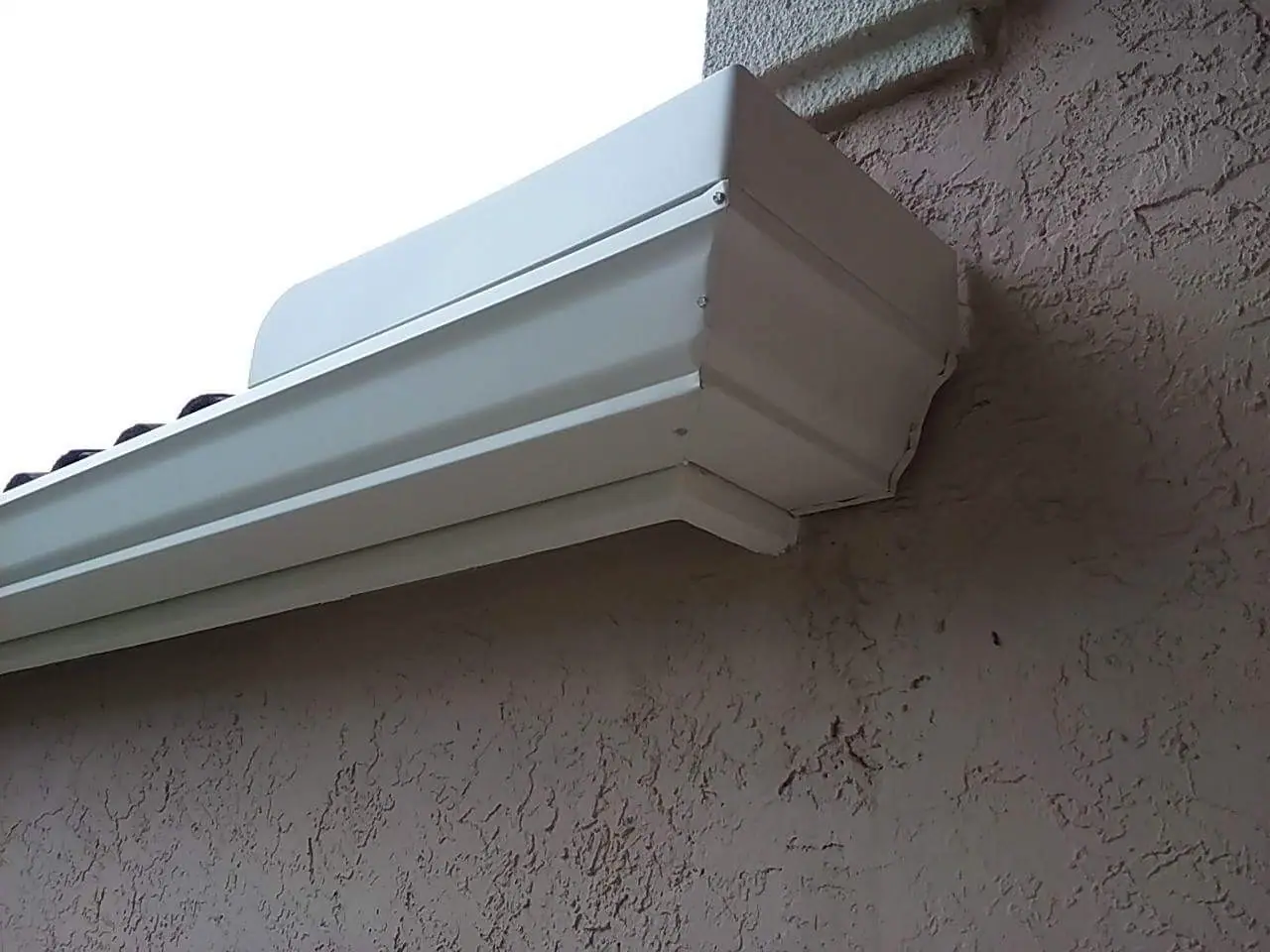 Close view of a white K-style gutter end cap on a stucco wall