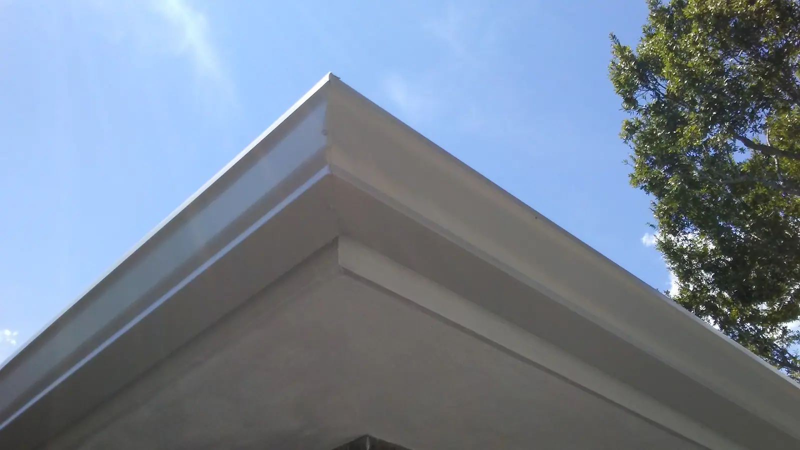 Mitred corner of a white seamless gutter against a blue sky