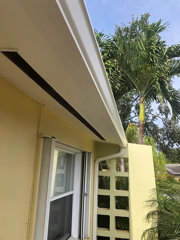 White gutter and downspout on a yellow stucco home with palm trees