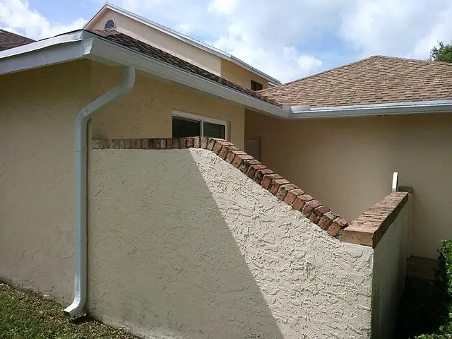 White downspout set into the corner of a beige stucco home